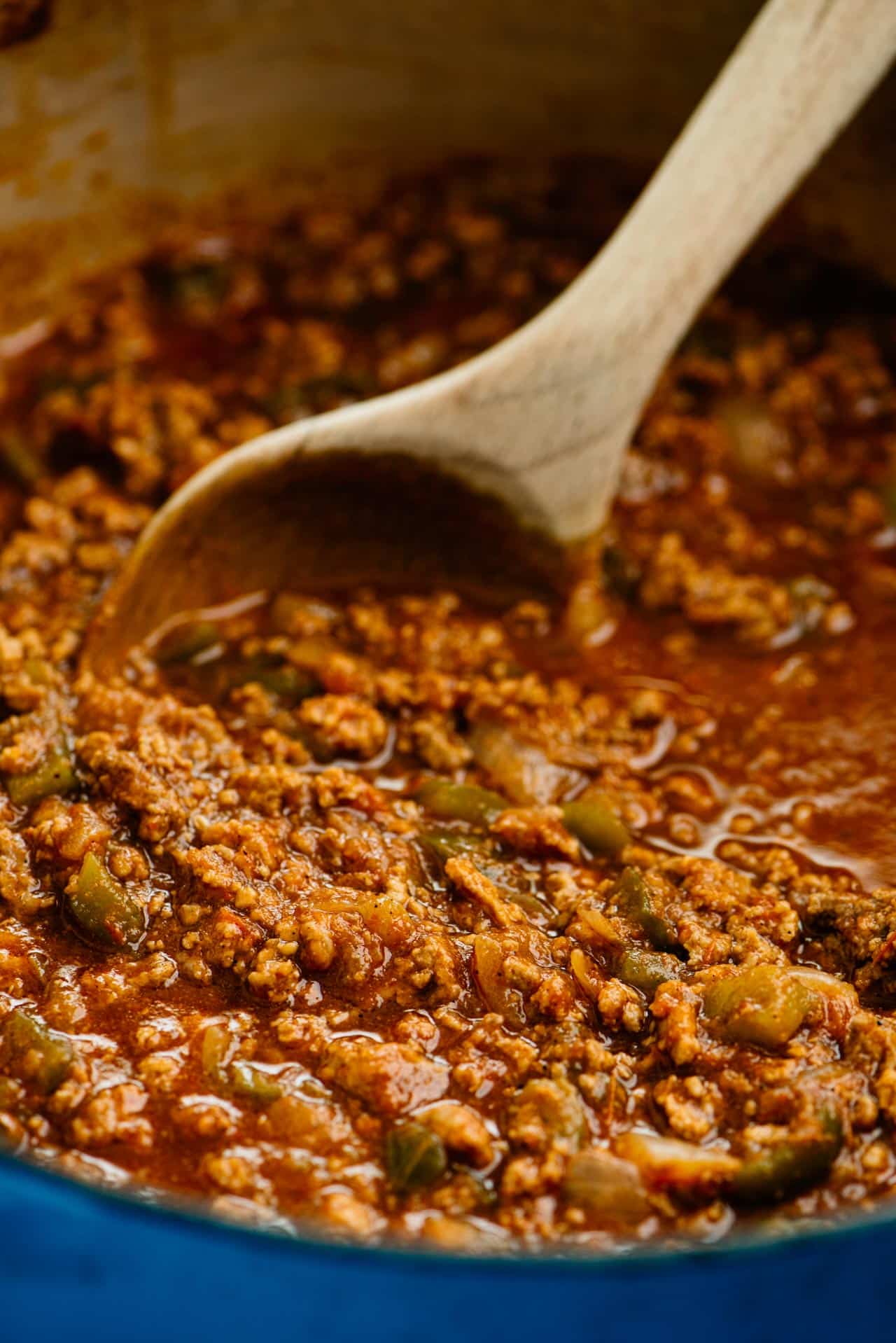 Stirring ground beef chili with a wooden spoon.