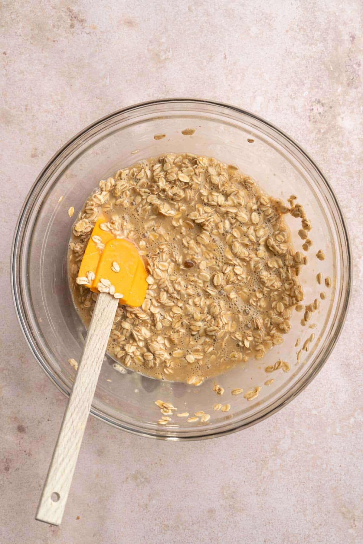 Stirring oats with milk, eggs, oil and brown sugar in a glass bowl.