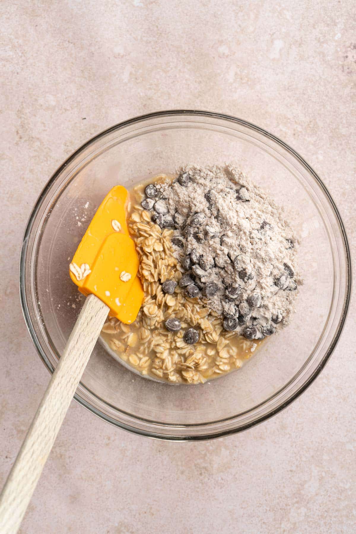 Stirring chocolate chips in flour with wet oat mixture.