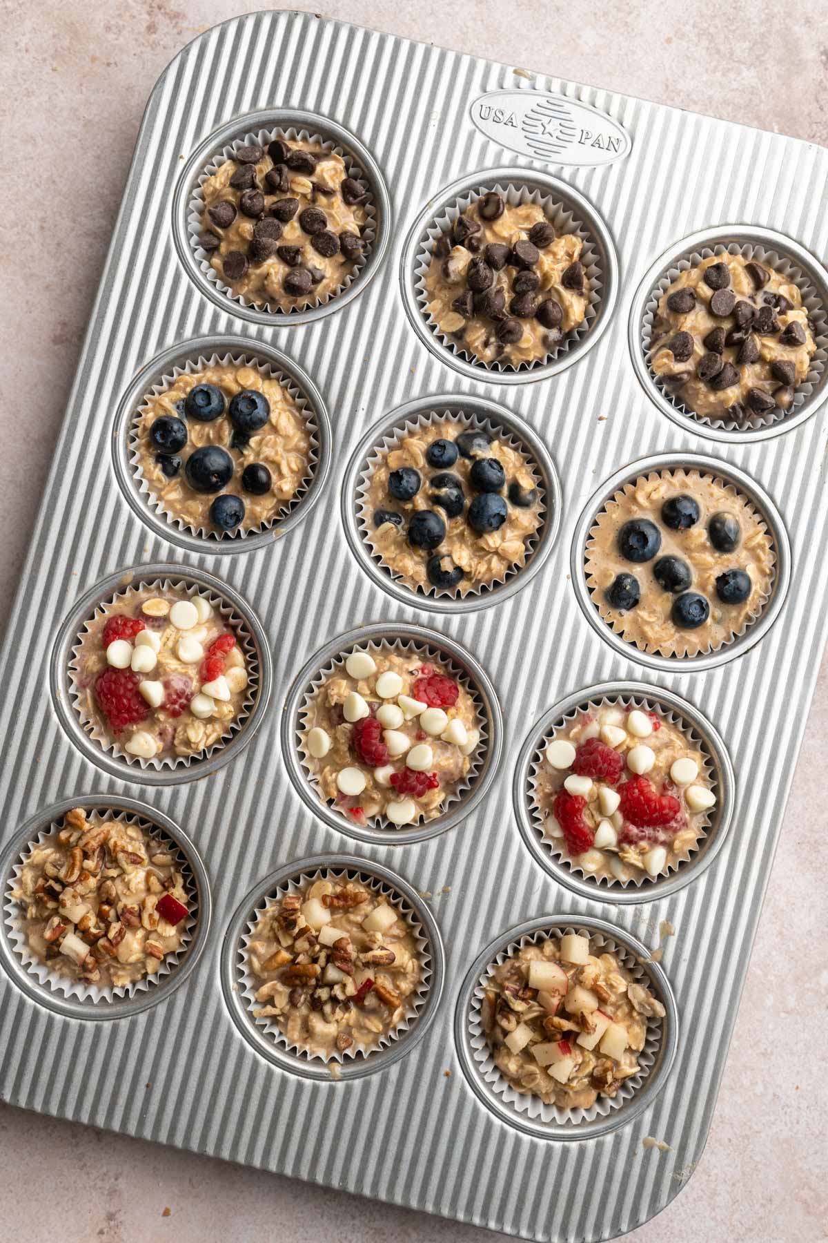 Muffin batter divided in a muffin pan and toppings added to the tops.