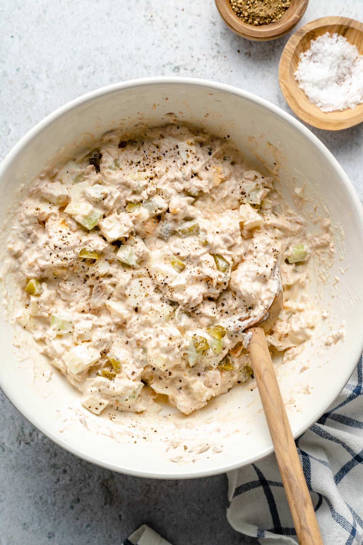 Stirring together tuna salad in a large white bowl.