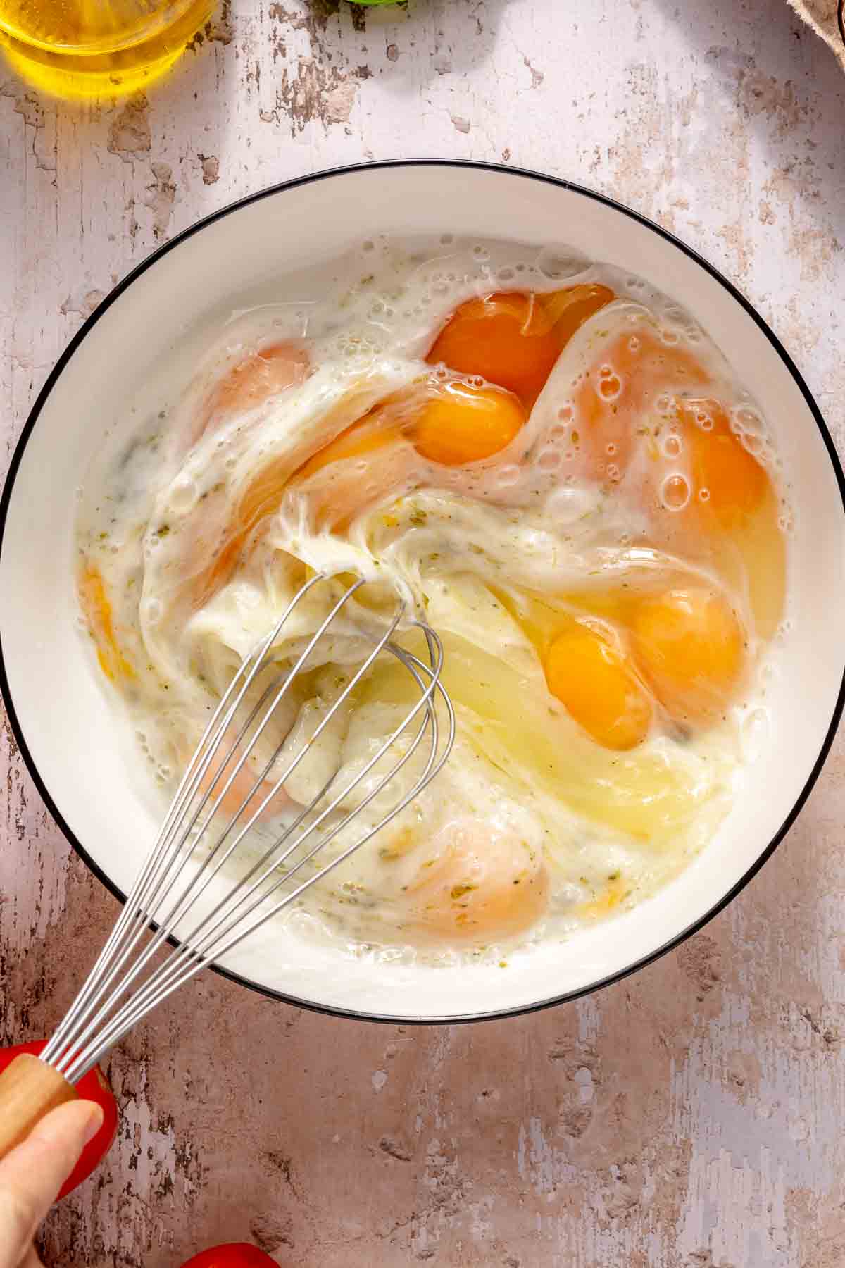 Whisking eggs with milk and pesto in a large bowl.