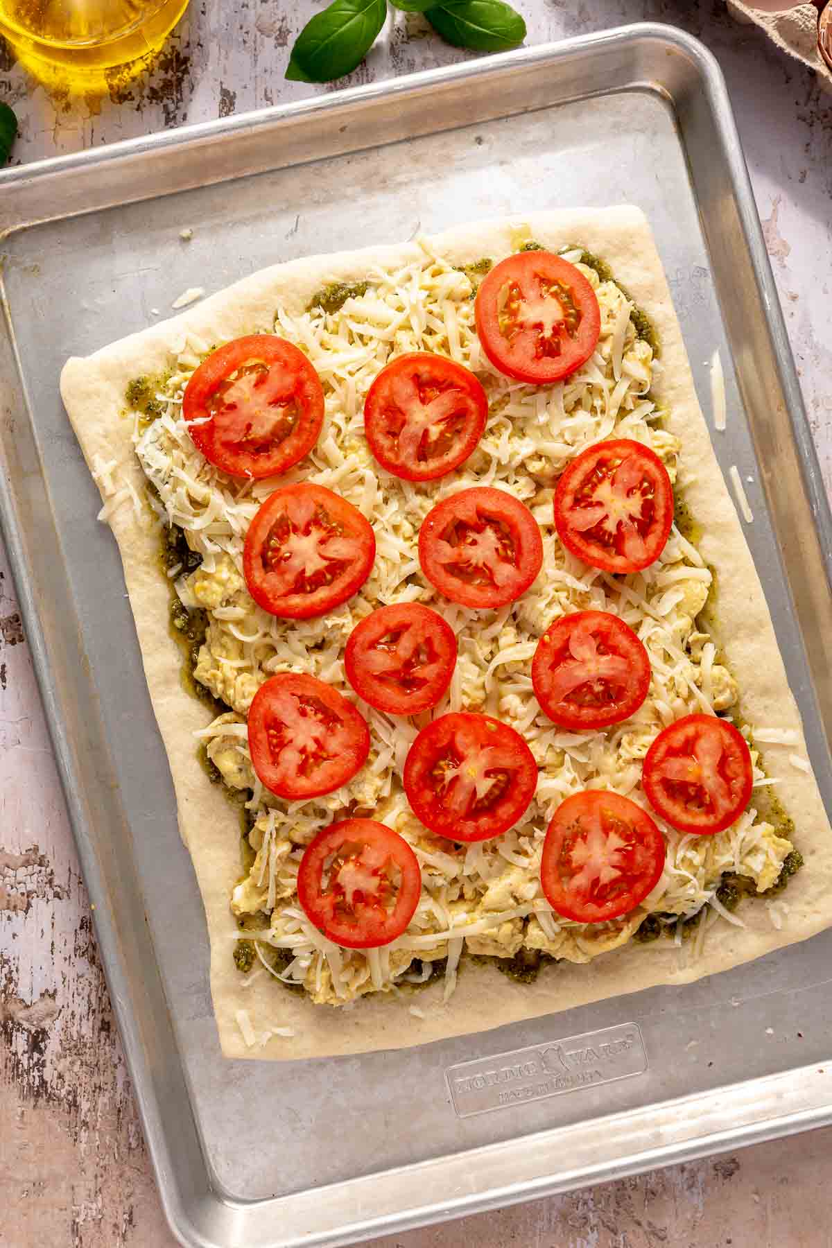 Pizza crust topped with pesto, eggs, cheese and tomatoes.