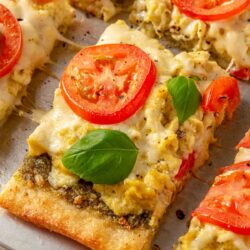 Breakfast pizza topped with fresh basil and sliced tomato.