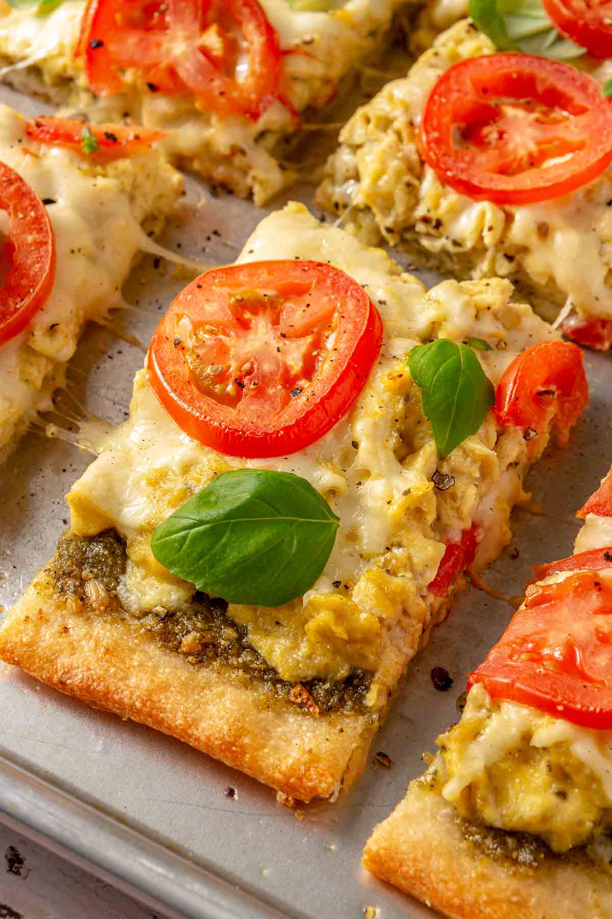 Breakfast pizza topped with fresh basil and sliced tomato.