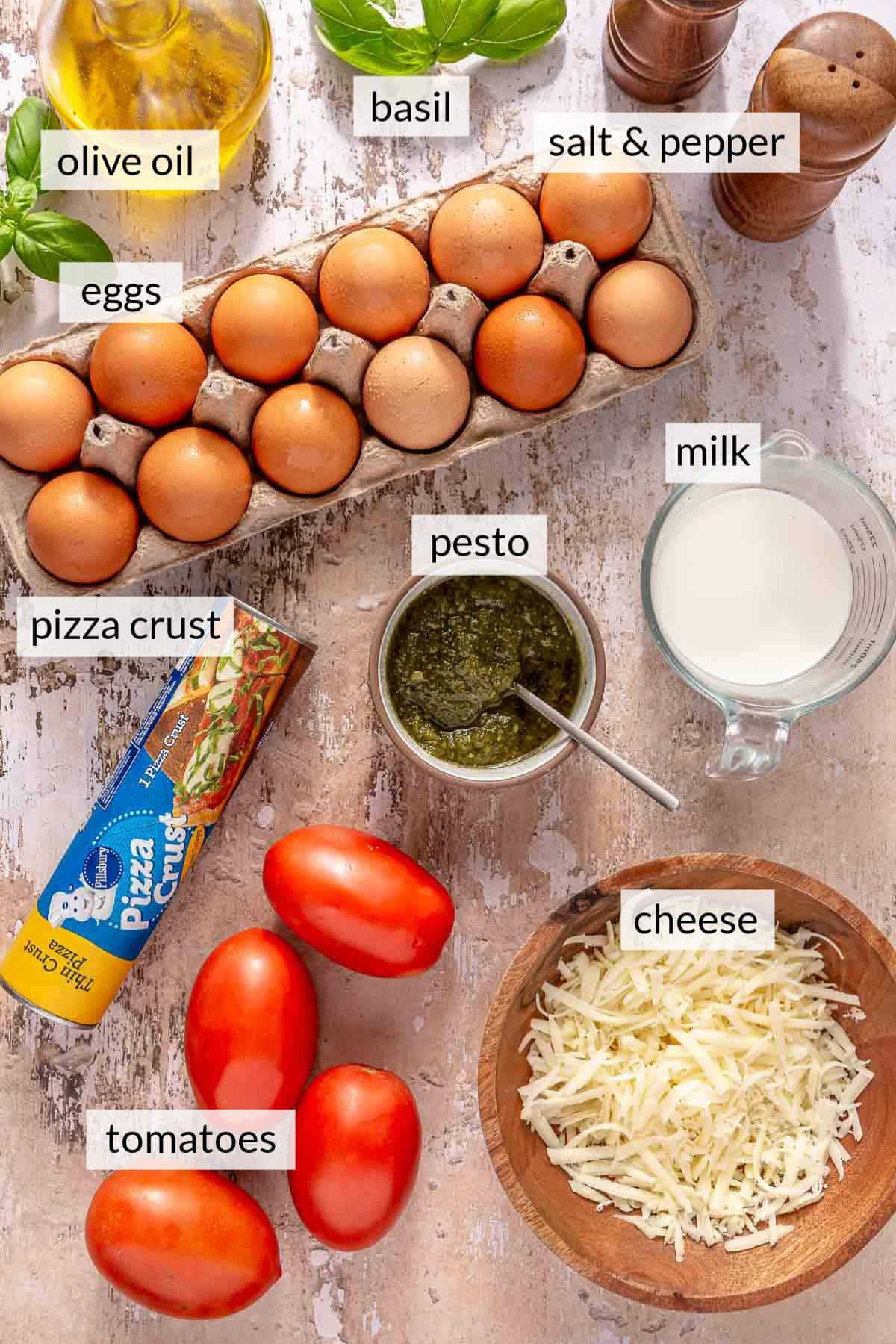 Carton of eggs near tomatoes, a tube of pizza crust, and bowls of cheese and pesto.