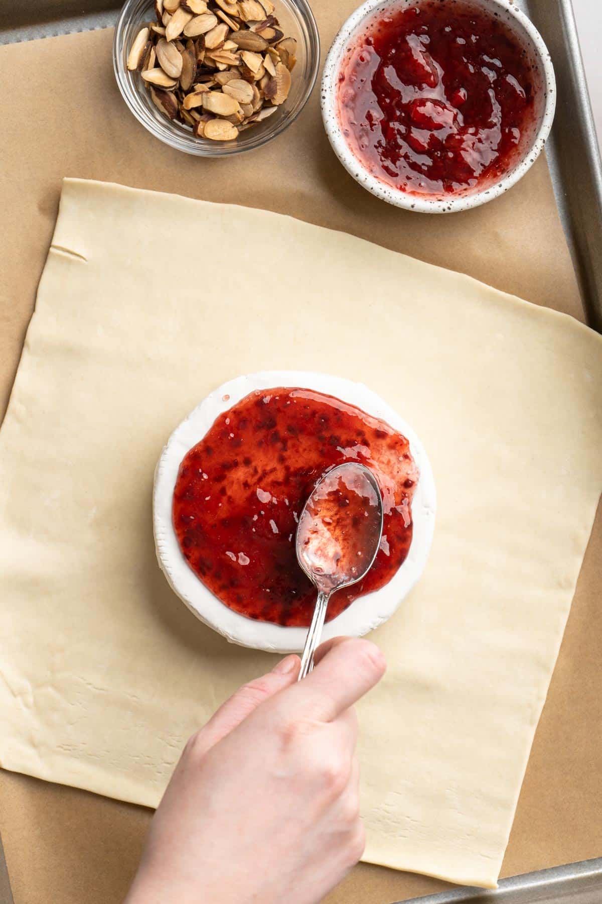 Spreading raspberry preserves on a brie cheese round.