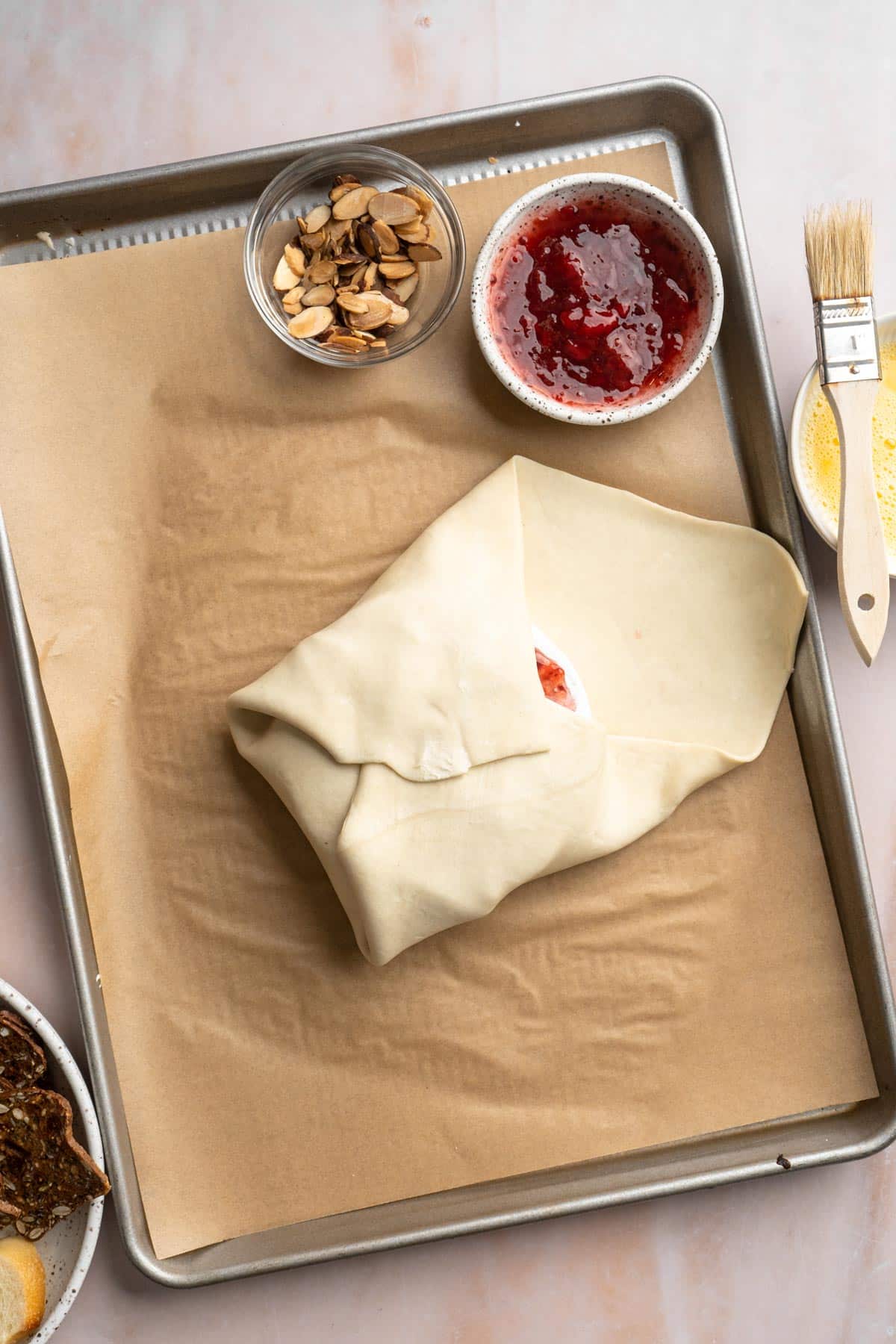 Folding puff pastry over brie on a baking sheet.