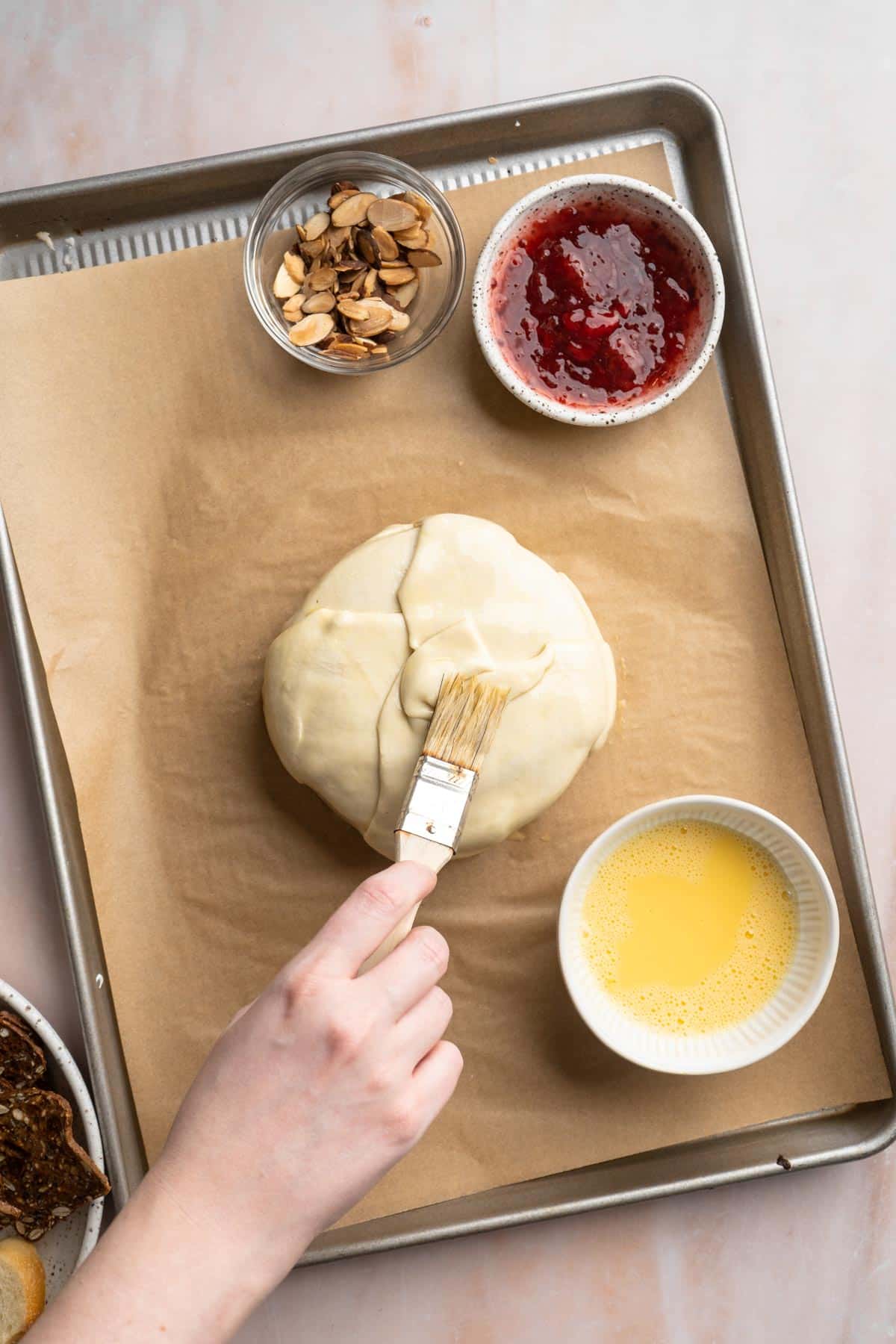 Brushing an egg wash over a puff pastry wrapped around cheese.