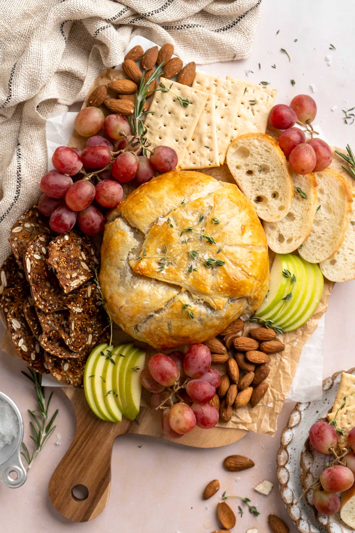 Baked Brie in puff pastry on a board with grapes, apple slices and crackers.