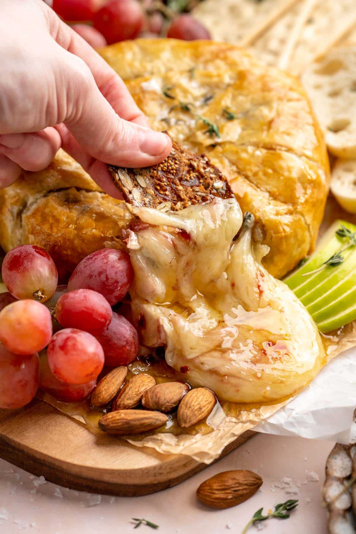 Hand dipping a cracker into melted Baked Brie.