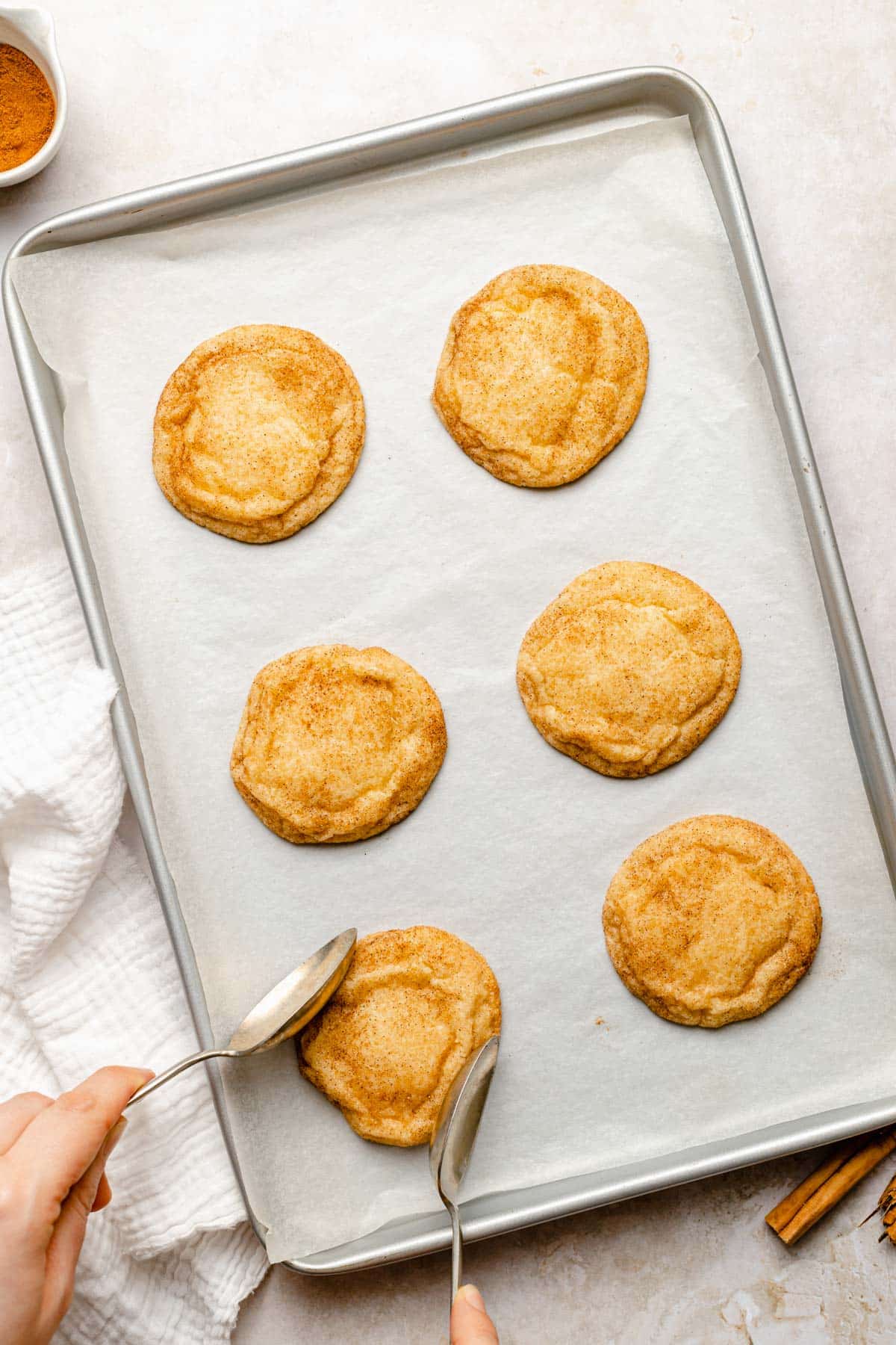 using spoons to press in the sides of snickerdoodle cookies