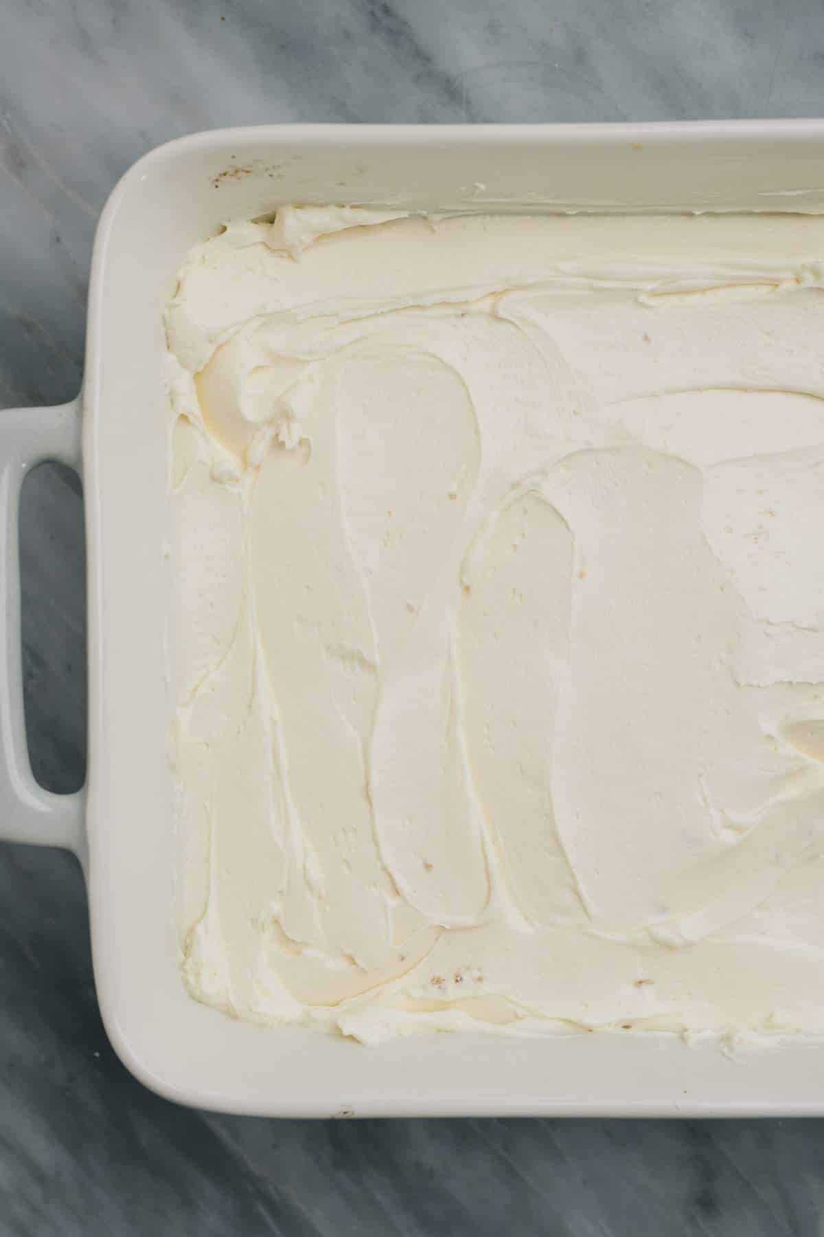 Cream cheese spread over crust in a white casserole dish.