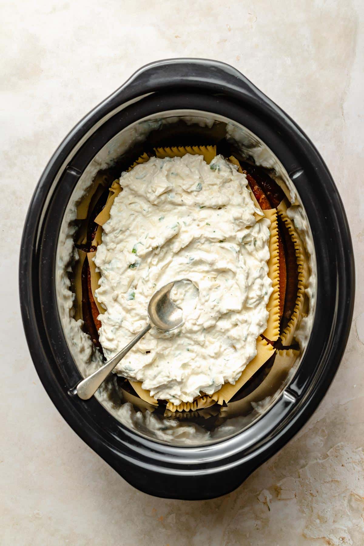 Topping lasagna noodles with cheese sauce in a crockpot.