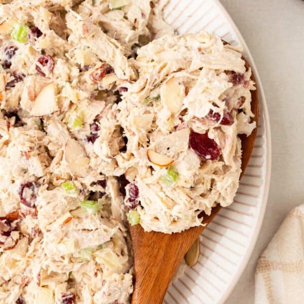 Serving healthy chicken salad with a wooden spoon out of a white bowl.