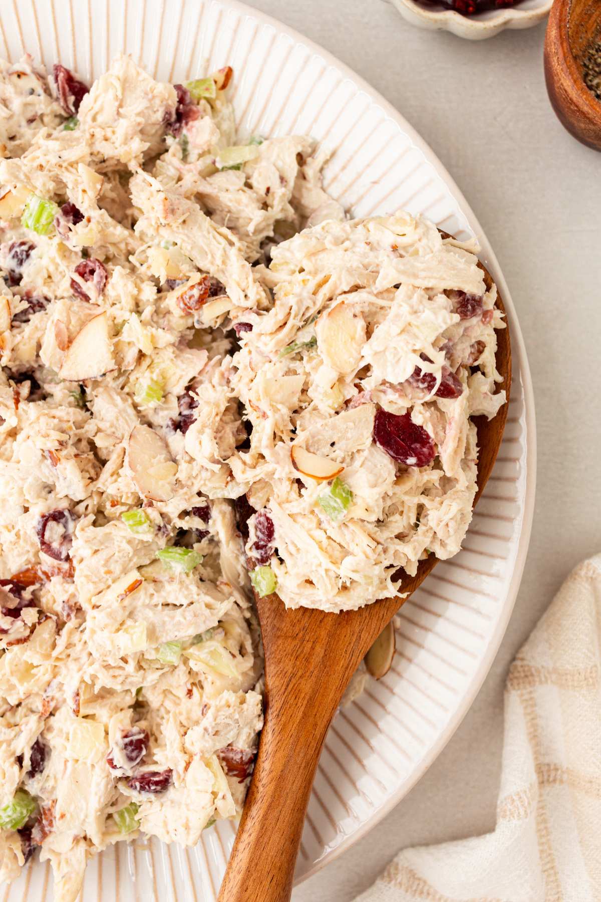 Serving healthy chicken salad with a wooden spoon out of a white bowl.