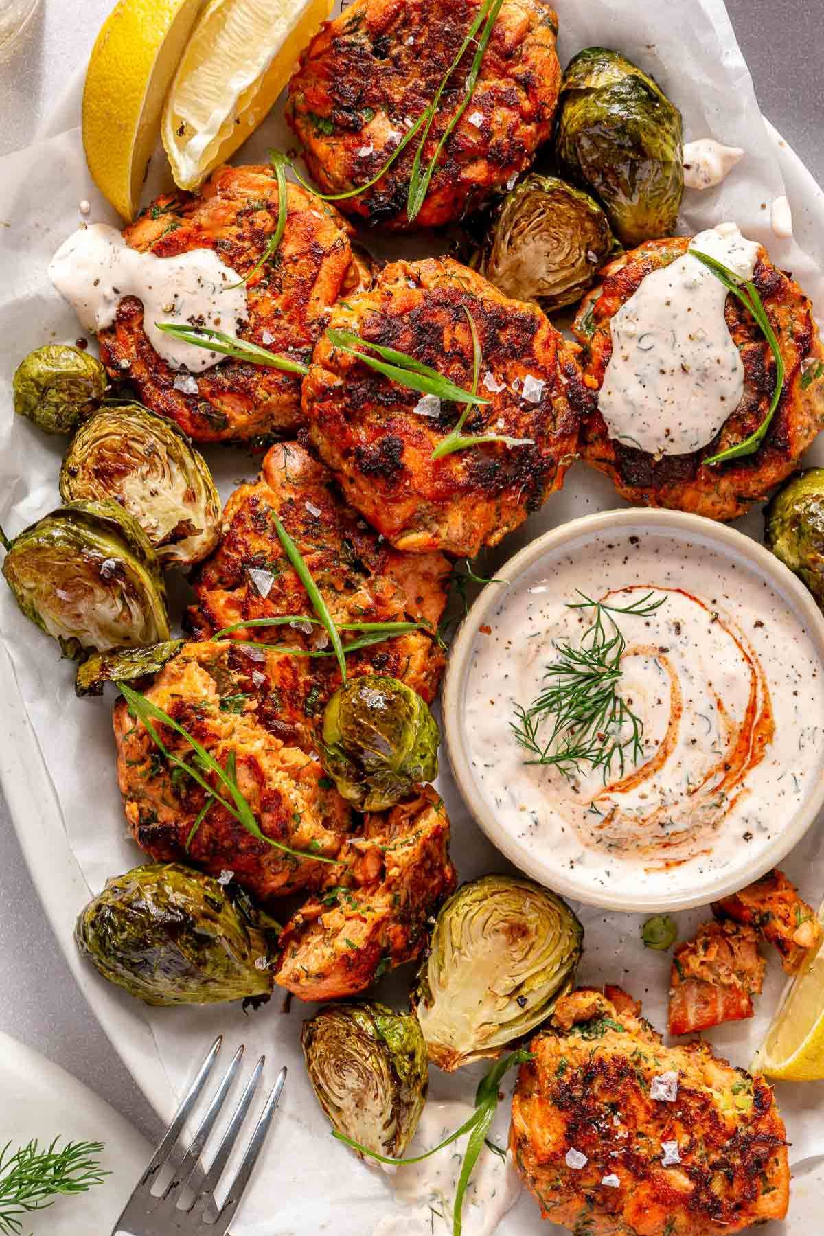 Salmon cakes served with creamy sauce, Brussels sprouts and lemon wedges.