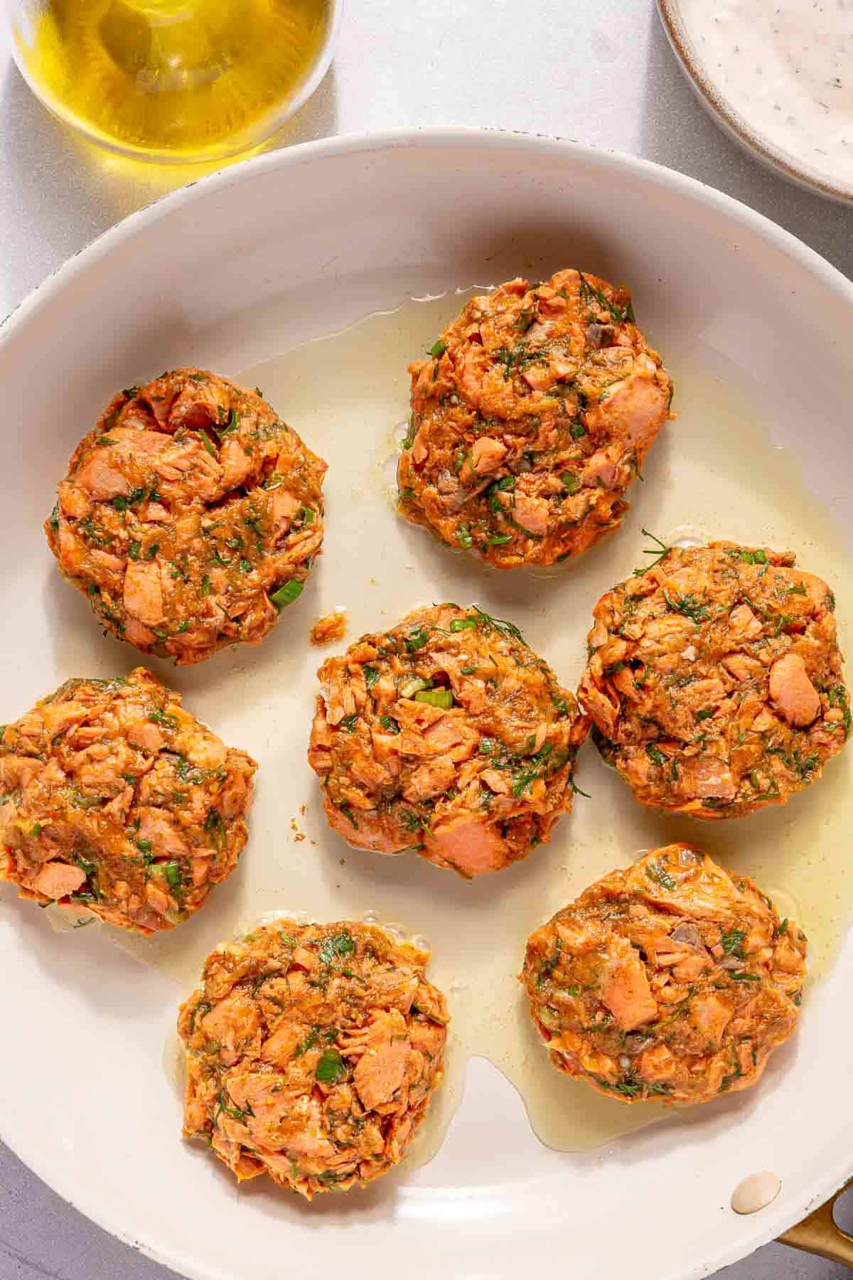 Cooking salmon cakes in a skillet with olive oil.