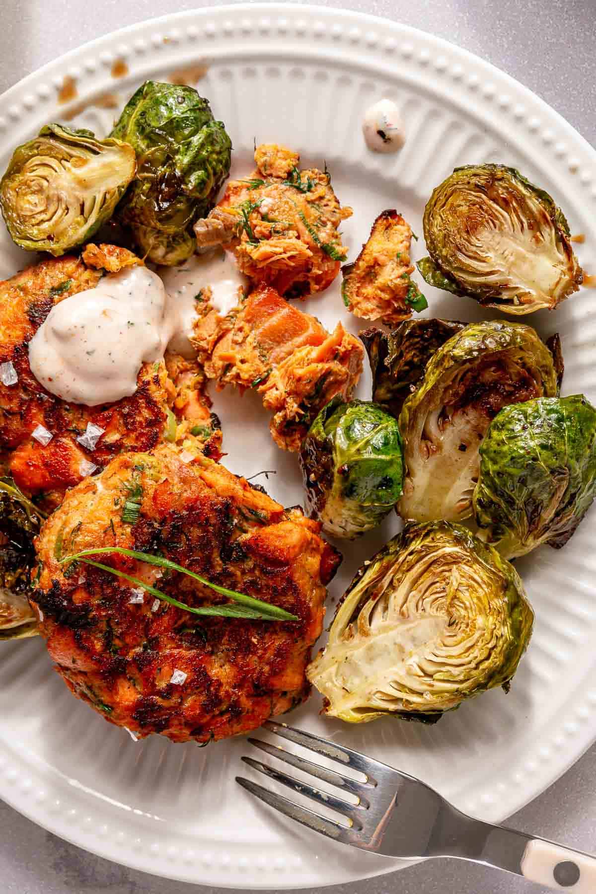 Salmon cakes and Brussels sprouts served on a white plate.