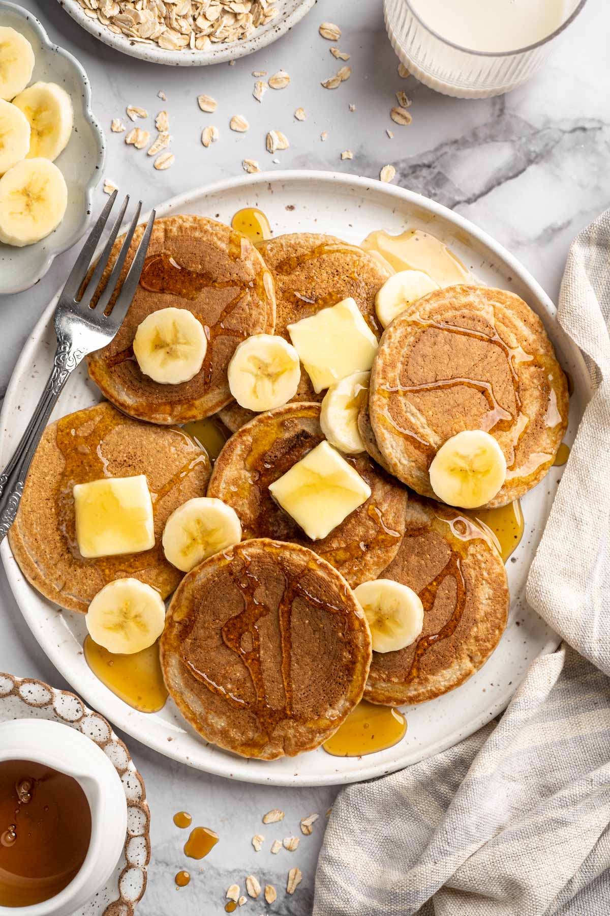 Banana oatmeal pancakes on a plate with butter, banana slices and syrup.