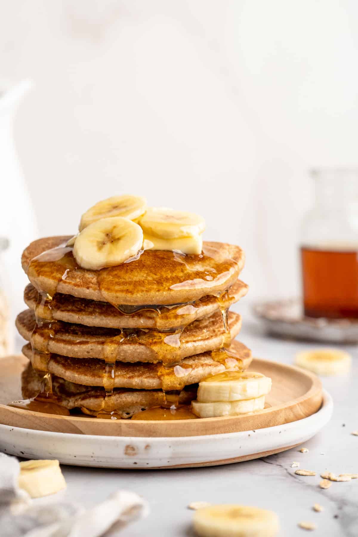 A stack of banana oatmeal pancakes topped with banana slices, butter and maple syrup.