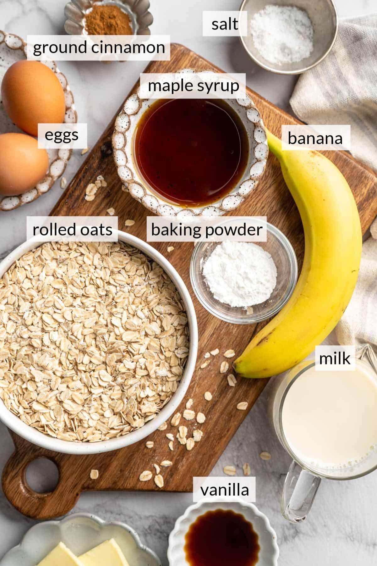 Bowls with rolled oats, maple syrup, vanilla, and milk near a banana and eggs. 