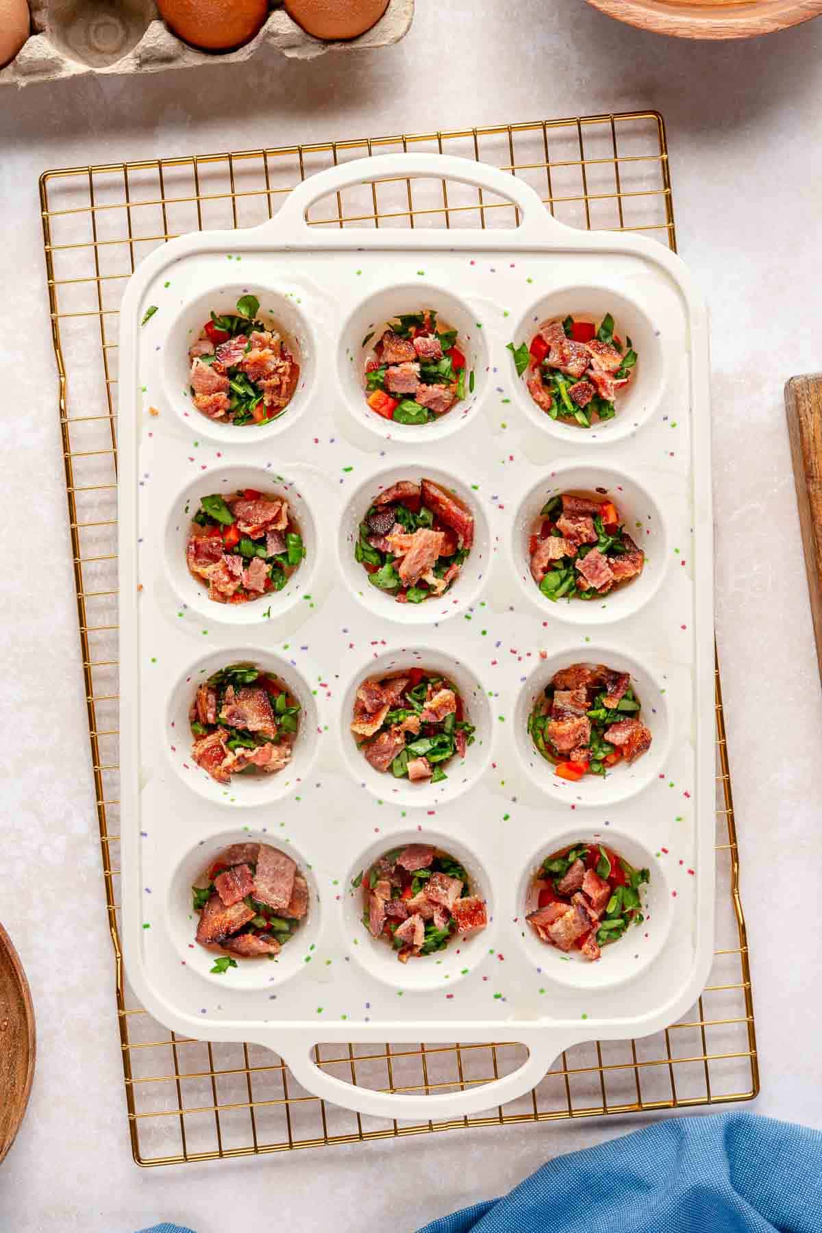 Chopped bell pepper, spinach and bacon added to a muffin pan.