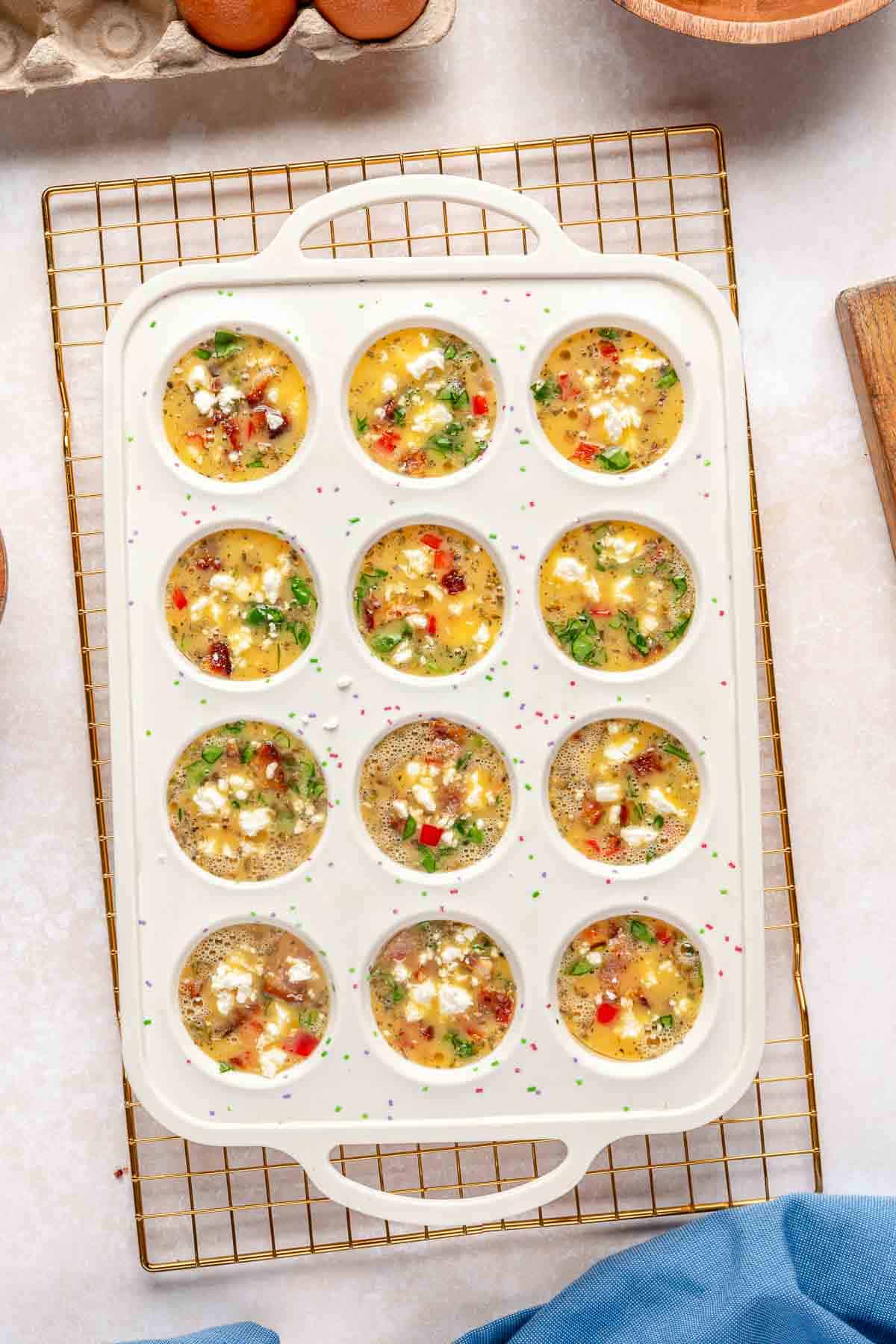 Eggs in a muffin pan with veggies and crumbled feta.