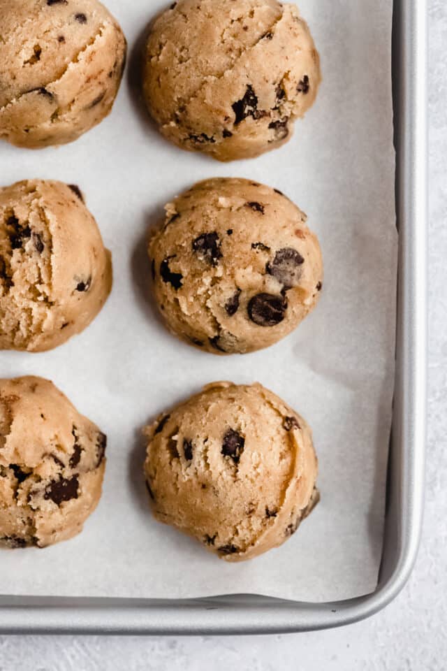 Balls of chocolate chip cookie dough on a baking sheet.