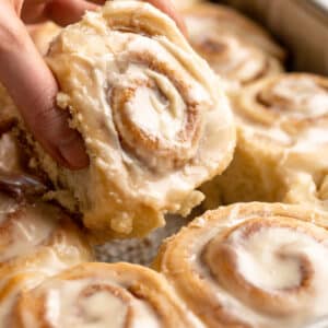 Pulling an iced cinnamon roll out of a baking pan.