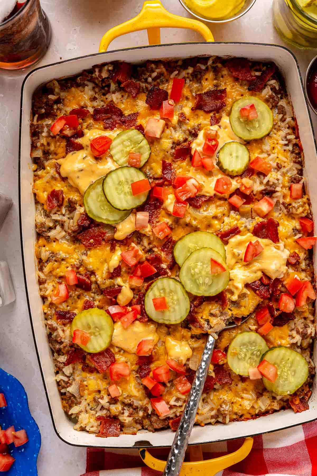 Cheeseburger casserole topped with pickle slices, diced tomatoes and bacon.