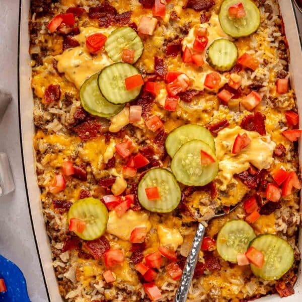 Cheeseburger casserole topped with pickle slices, diced tomatoes and bacon.