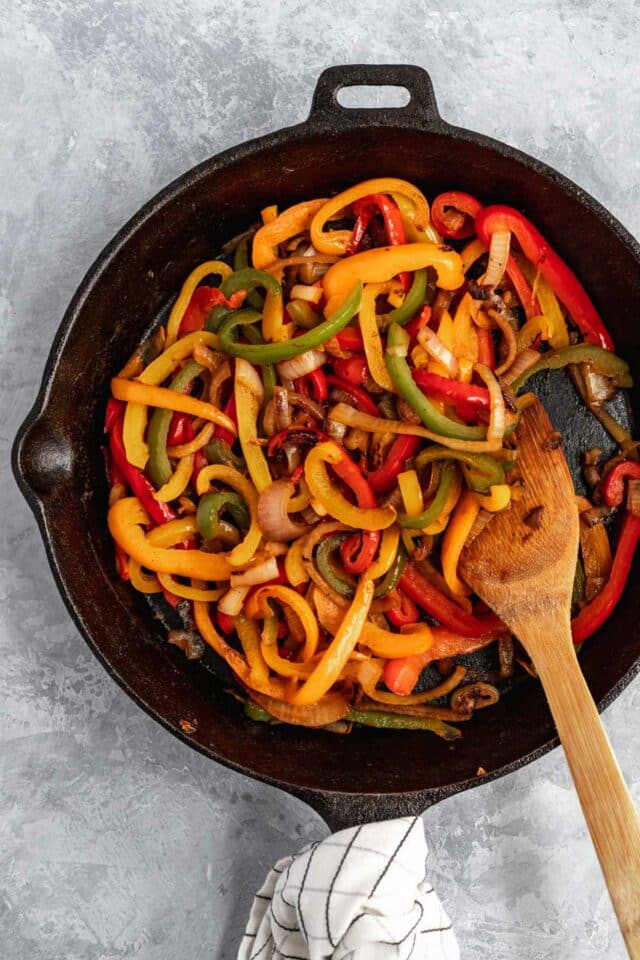 Cooking peppers and onion in a large pan.