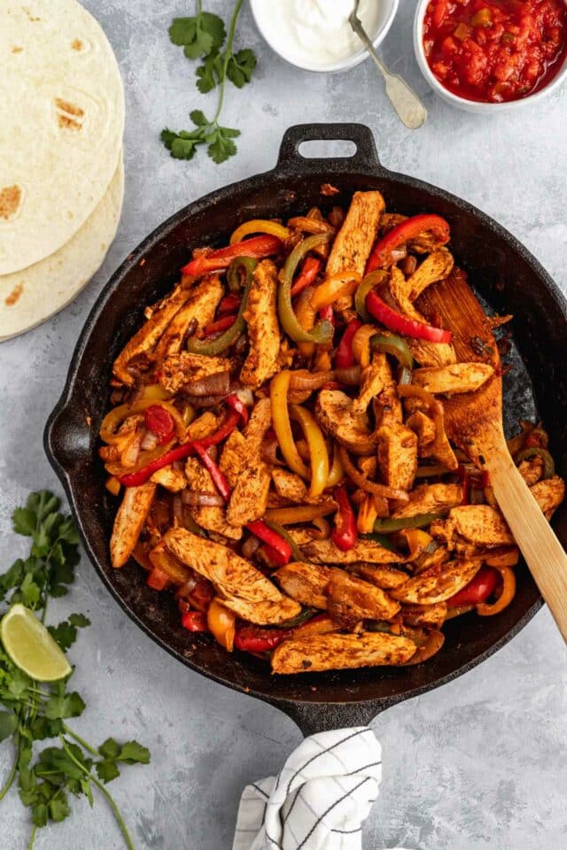 Stirring together sliced chicken with bell pepper and onion in a cast iron skillet.