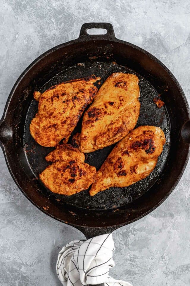 Chicken breasts cooking in a cast iron skillet.