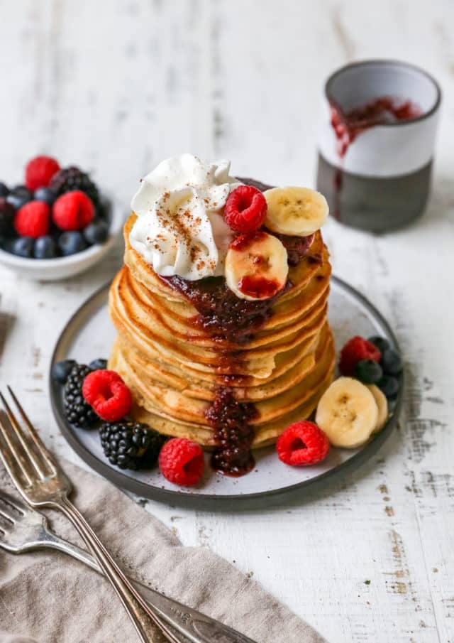 pancakes stacked on a plate with fruit syrup and whipped cream