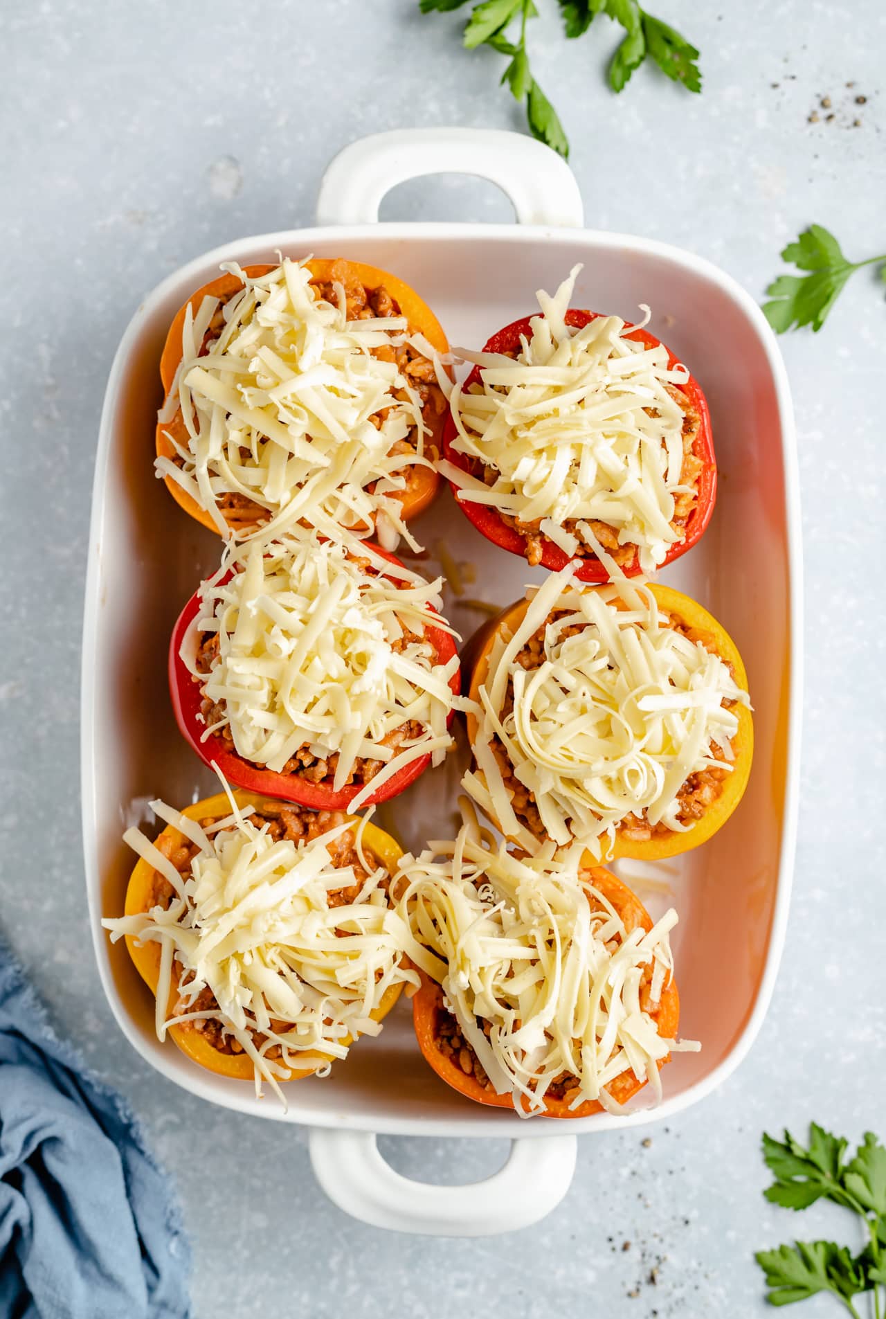 Topping bell peppers with shredded cheese before baking.