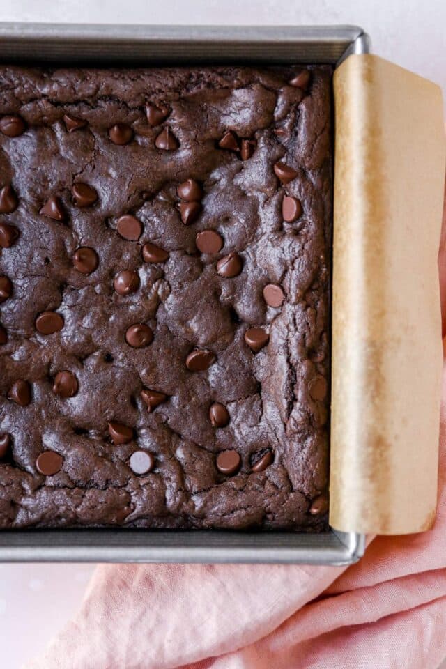 Cooked brownies in a pan lined with parchment paper.