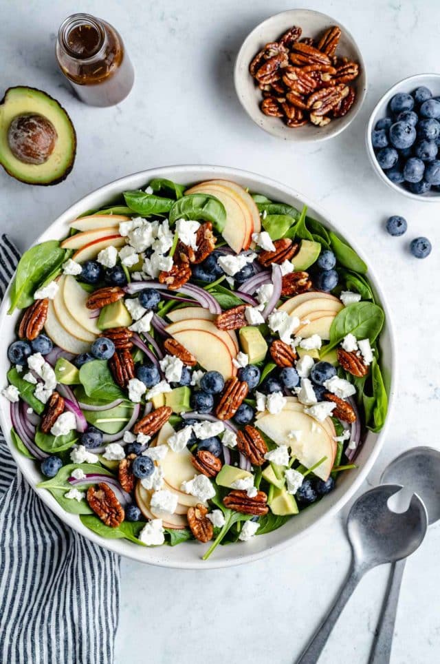 spinach salad topped with apple slices, blueberries and feta cheese