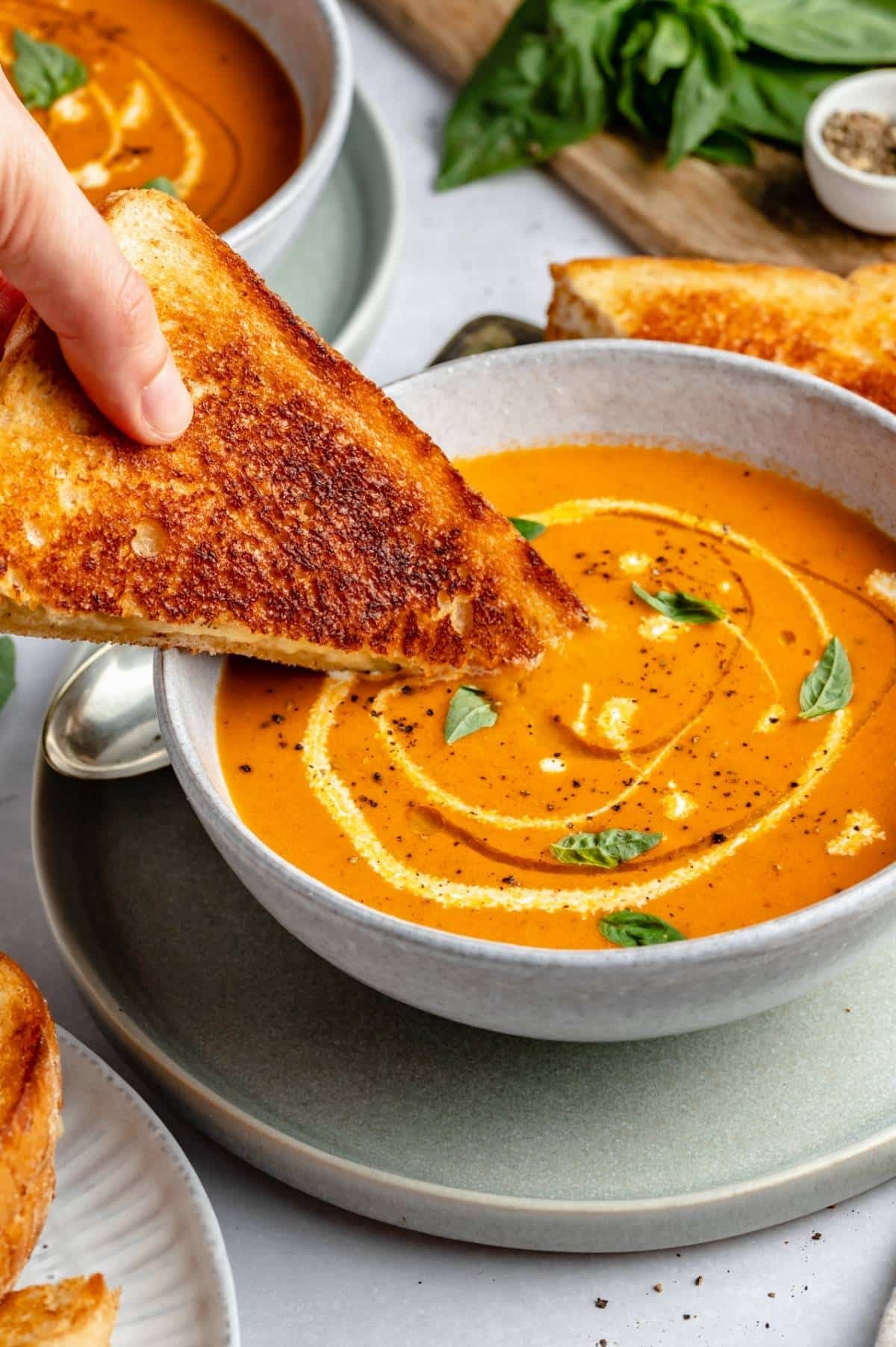 hand dipping a grilled cheese sandwich into tomato soup