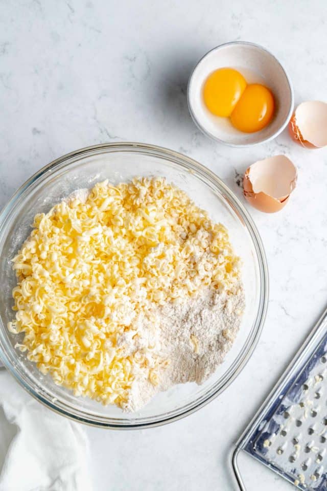 Grated butter in a bowl with flour and another smaller bowl with eggs.