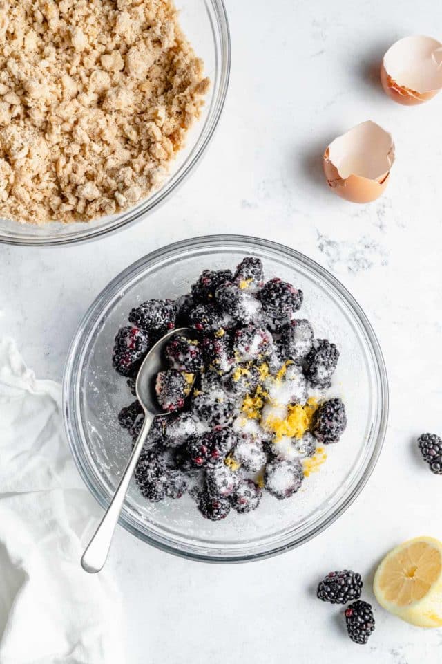 Using a spoon to combine blackberries with lemon zest and sugar in a small bowl.