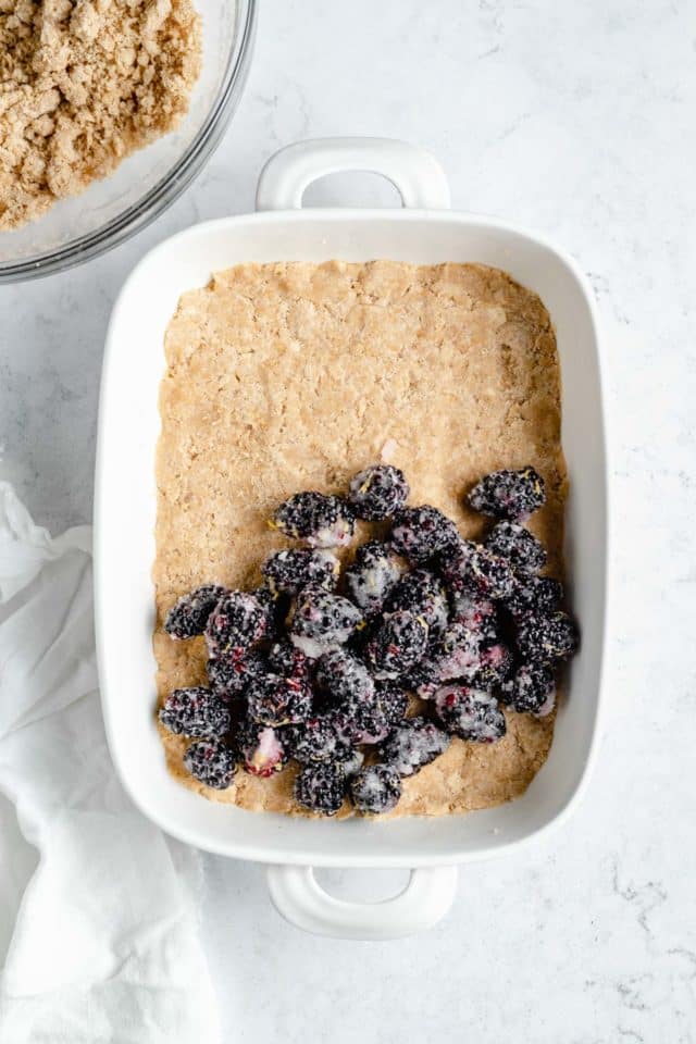 Assembling a blackberry crumble with a crust and blackberries in a dish.