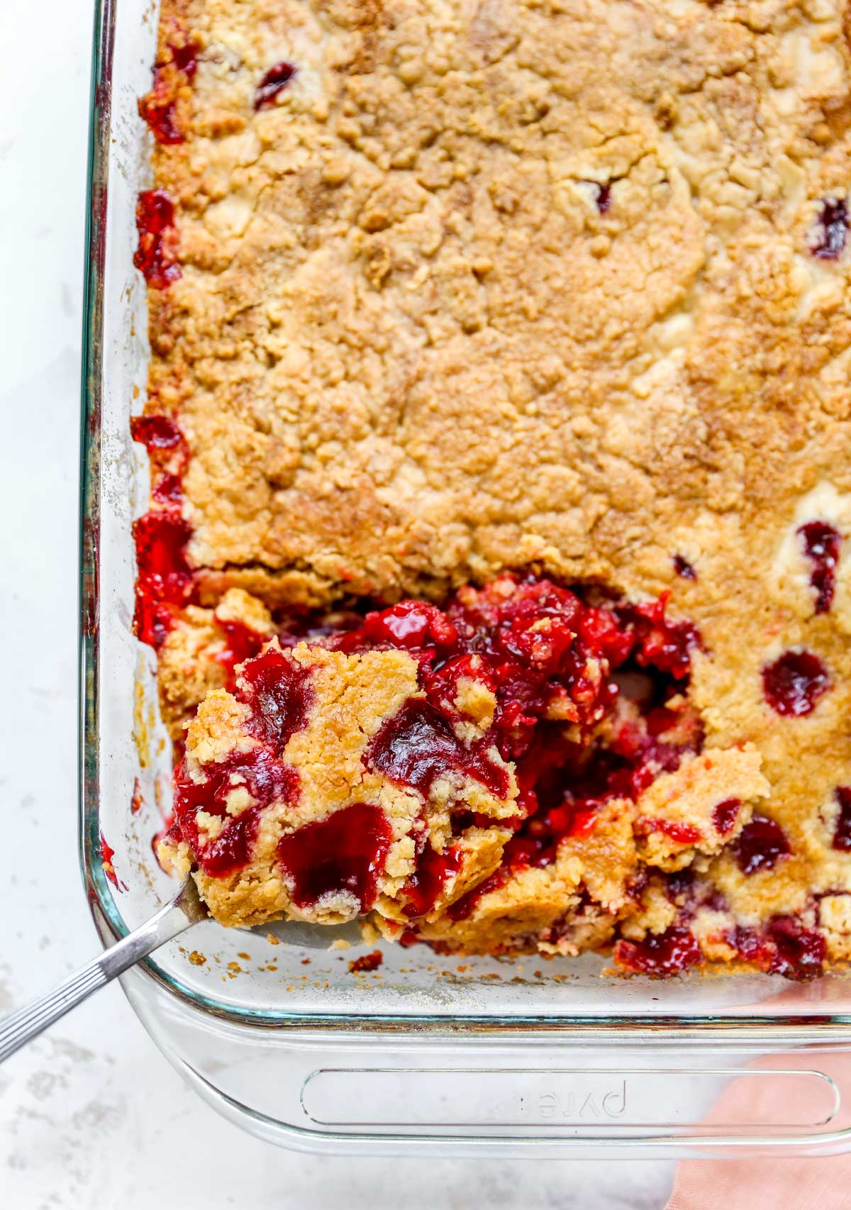 Scooping a serving of cherry dessert out of a glass baking dish.