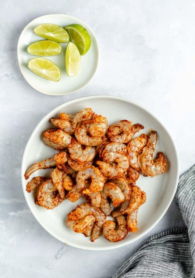 raw seasoned shrimp in a white bowl near fresh lime wedges