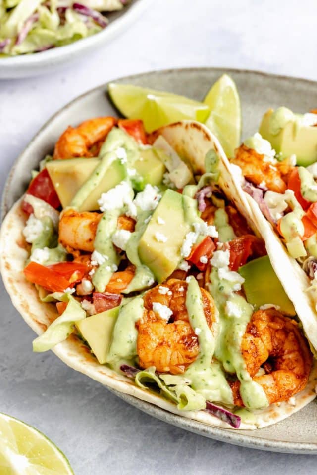 shrimp tacos served in flour tortillas with a drizzle of avocado sauce and cojita cheese