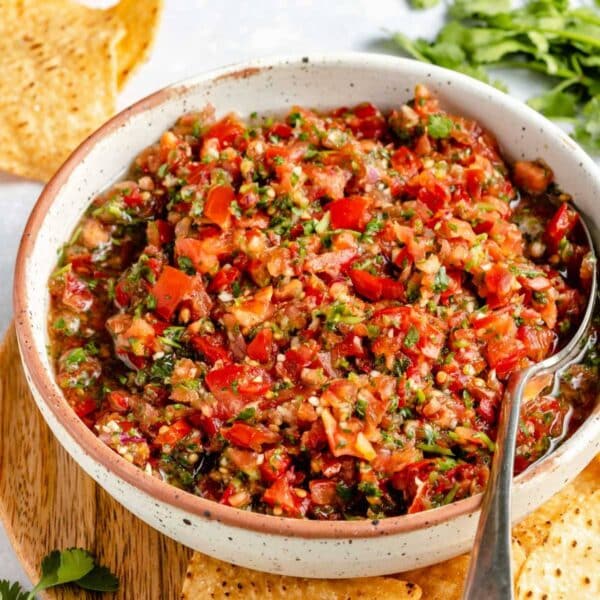 Homemade salsa served in a small white bowl with a spoon near chips.