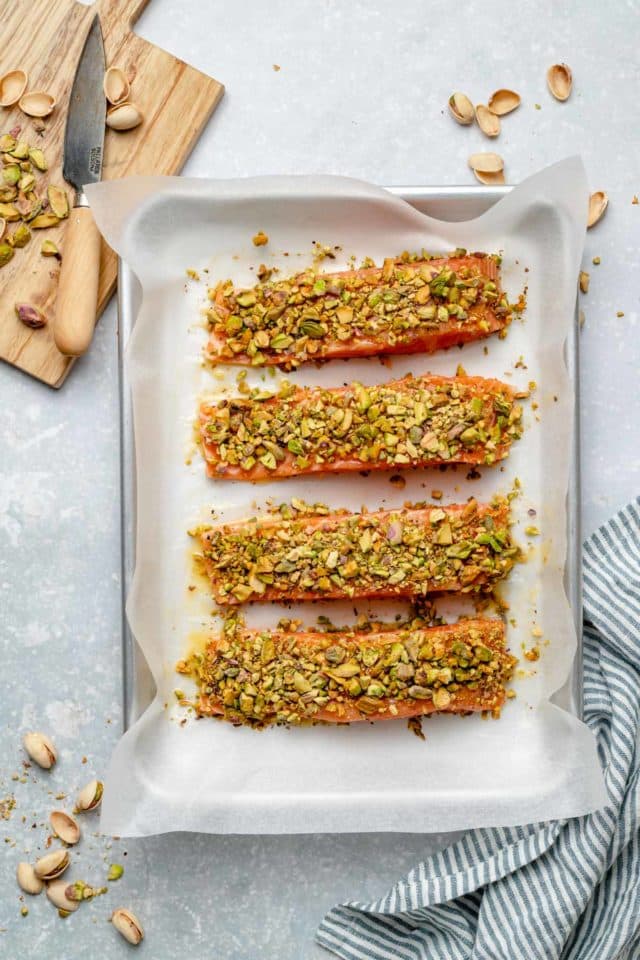 uncooked salmon topped with chopped pistachios on a baking sheet pan