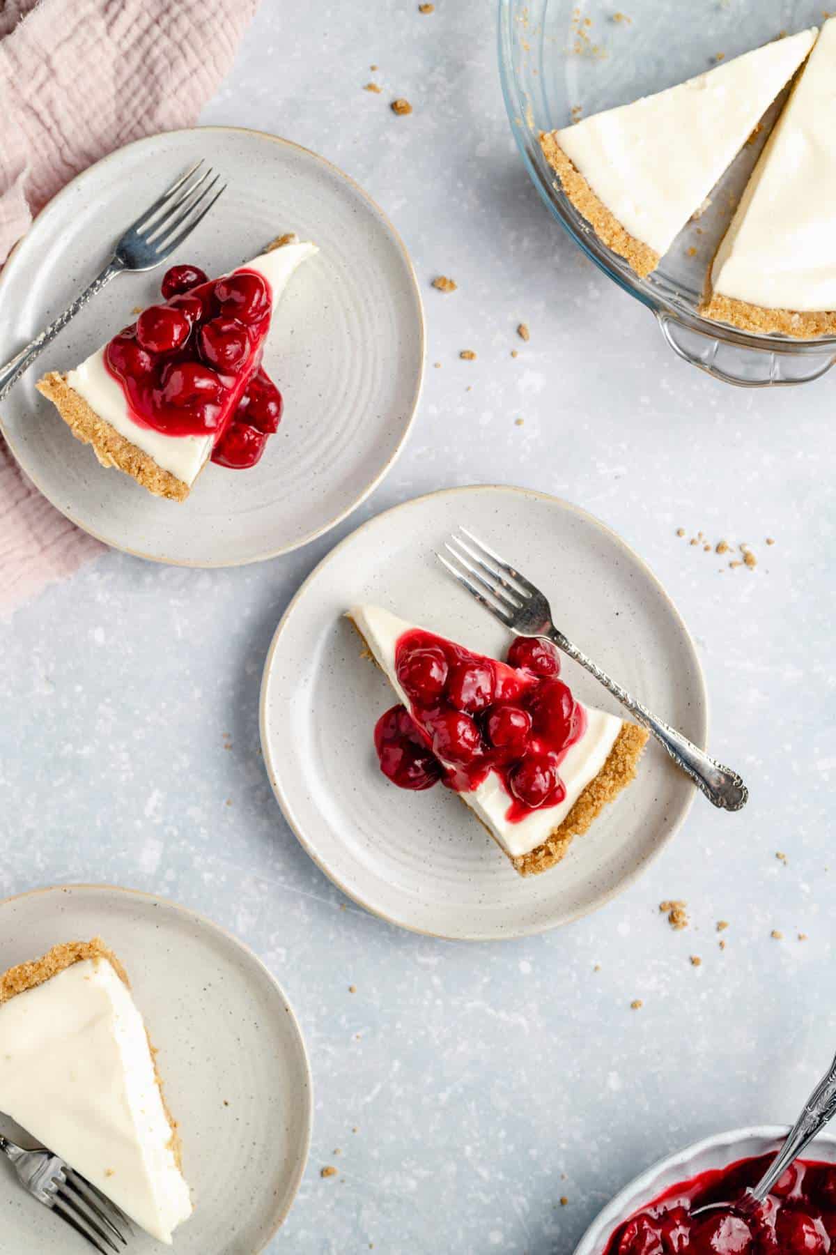 Slices of cheesecake topped with cherries on white plates.