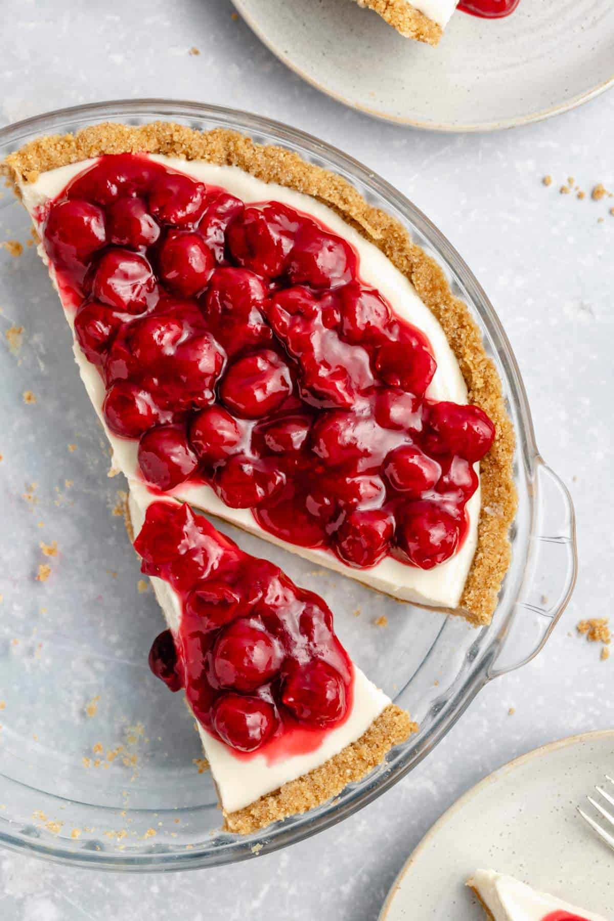 Sliced no bake cheesecake topped with cherry pie filling in a pie plate.